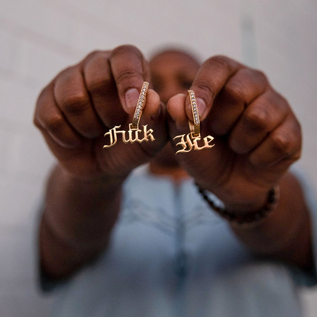 Model is holding Fuck ICE dangle earrings. Sterling Silver, 22k gold plated paved with cubic zirconia. Hoop dimensions: 1 in long x .5 inches Windells. Charm is removable.